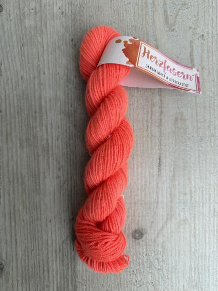 Strang aus 100 Prozent Kaschmir in leuchtendem Koralle-Neon mit Banderole Herzfasern auf hellem Holzuntergrund fotografiert.